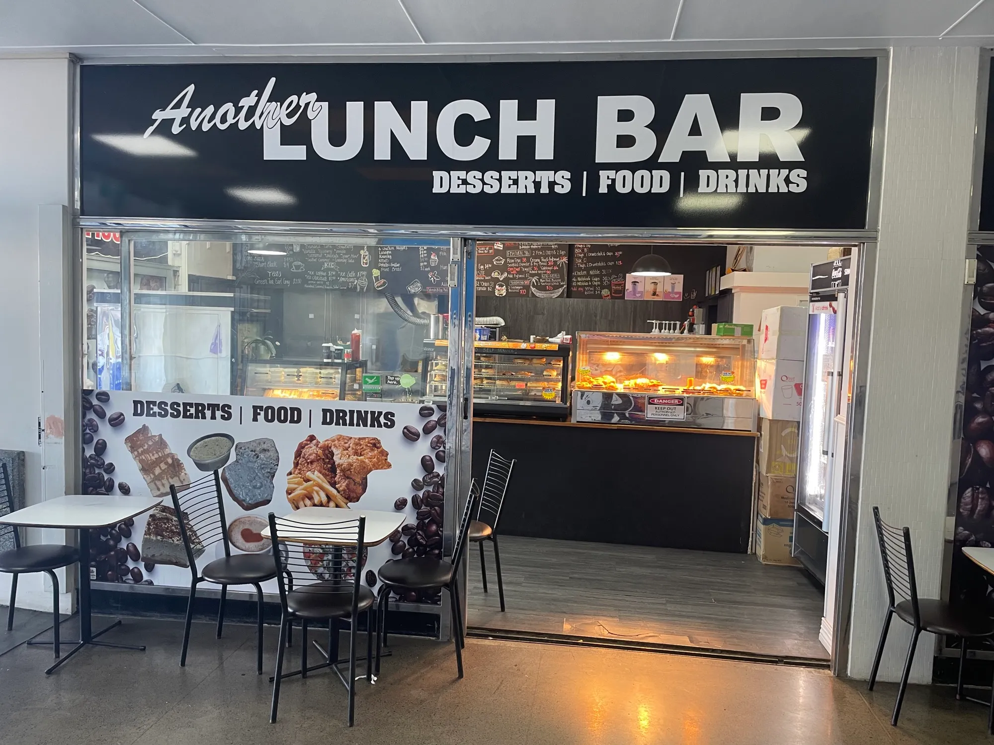 An open food counter at Southmall, its hot food cabinets lit up beneath handwritten menu boards, with tables and chairs set out in front.