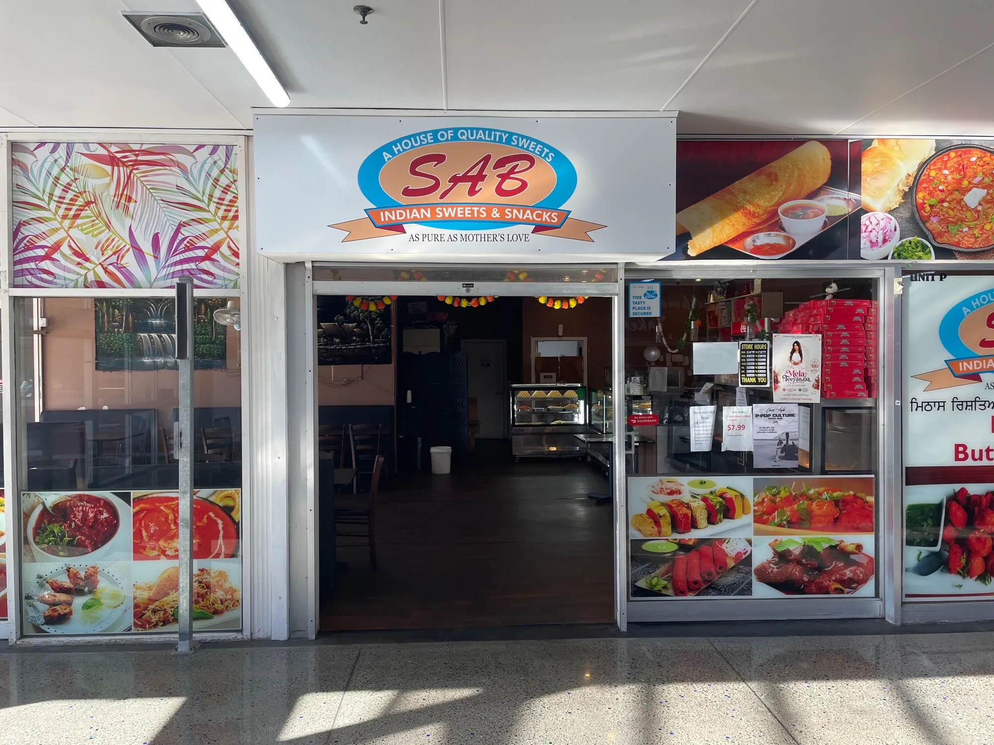 The SAB Indian Sweets & Snacks shopfront, its windows lined with photographs of curries and dosa, with a sweets cabinet visible inside.