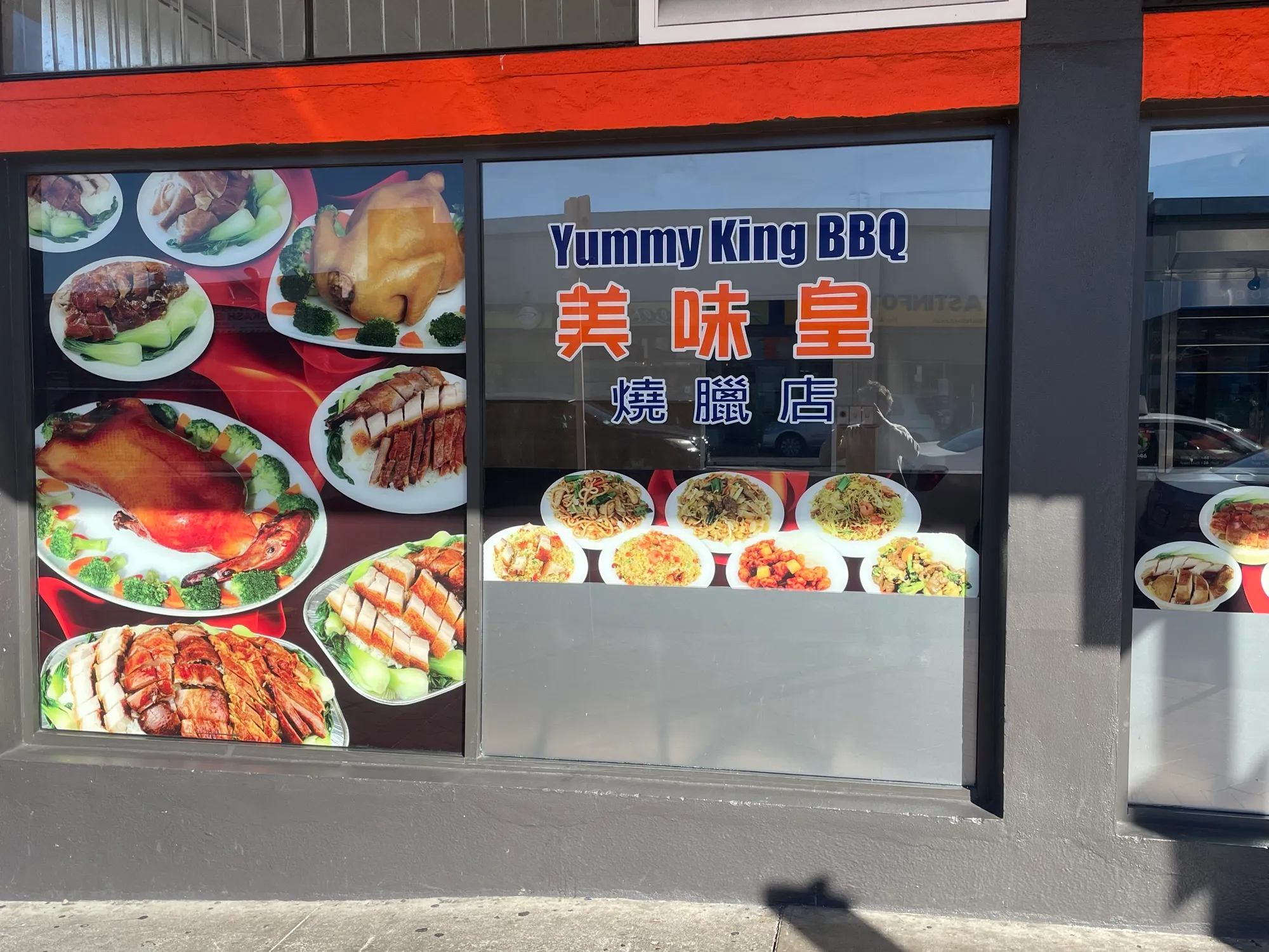 The Yummy King BBQ window, its glass lettered in English and Chinese and lined with photographs of roast duck, char siu, crispy pork, noodles and fried rice.