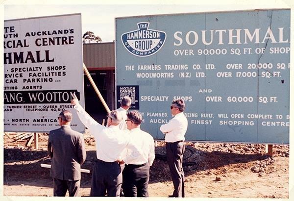 The covered walkway at Southmall, lined with shopfronts including Manurewa Post Lotto, its brick paving leading out to the sunlit entrance.